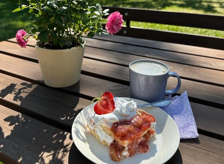 Pöydällä on ruusukukkapurkki, kakkulautanen ja kupillinen kahvia.