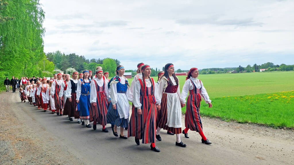 Kalevalaisia helkavirsiä laulava neitojen kulkue.