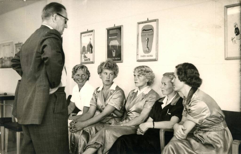 Viisi naista istuu sohvalla ja heidän edessään seisoo mies.