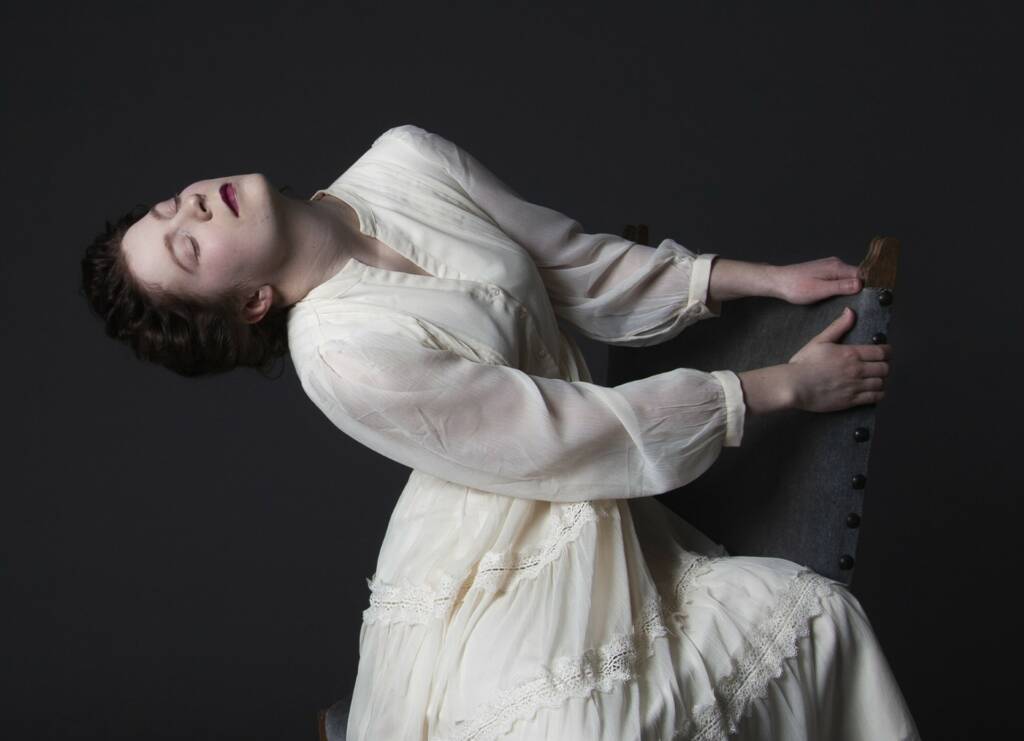 Valkohameinen nainen istuu taiteellisessa asennossa.