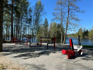 Ulkona järven rannalla erilaisia kuntosalilaitteita.