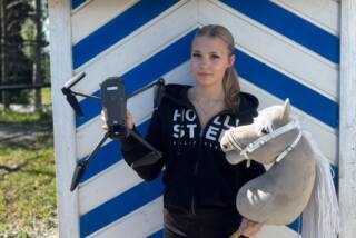 Tyttö pitää toisessa kädessään dronea ja toisessa kädessään keppihevosta.