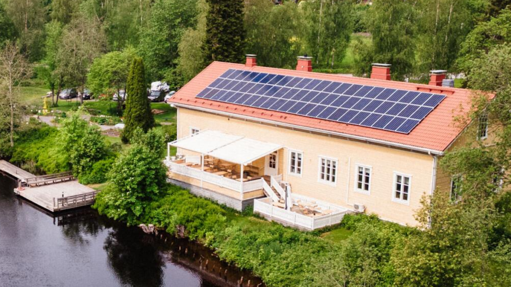 Keltainen talo järven rannalla. Aurinkopaneelit talon katolla.
